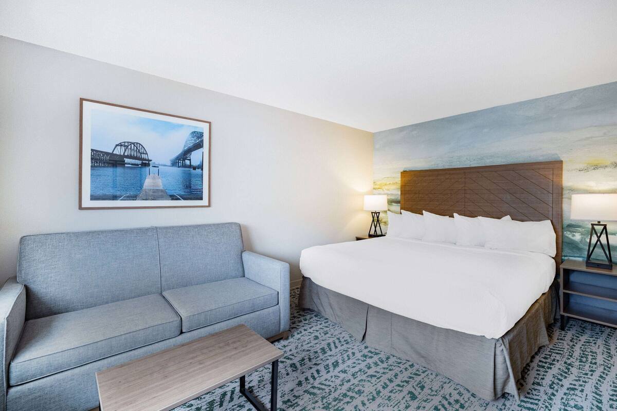 Hotelkamer met een bed, een bank, een tafeltje, een lamp en een schilderij van een brug.
