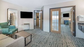 Une chambre d’hôtel avec un fauteuil vert, une petite table, un téléviseur à écran plat, une cheminée et un miroir.