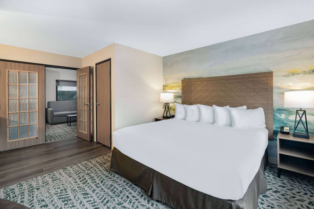 Een hotelkamer met een groot bed, een bureau met lamp, een stoel en een schilderij aan de muur.