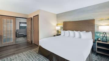 A hotel room with a large bed, a desk with a lamp, a chair, and a painting on the wall.