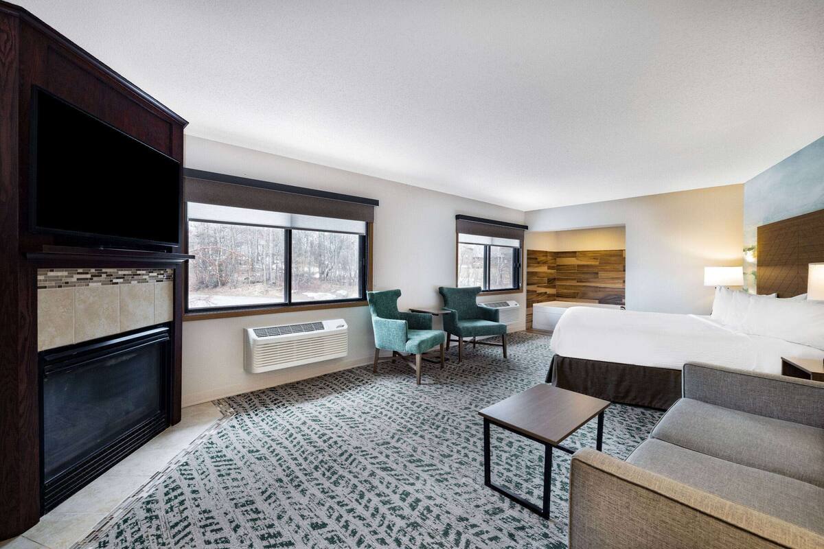 Een hotelkamer met een groot bed, twee fauteuils, een tafeltje, een televisie en een open haard.