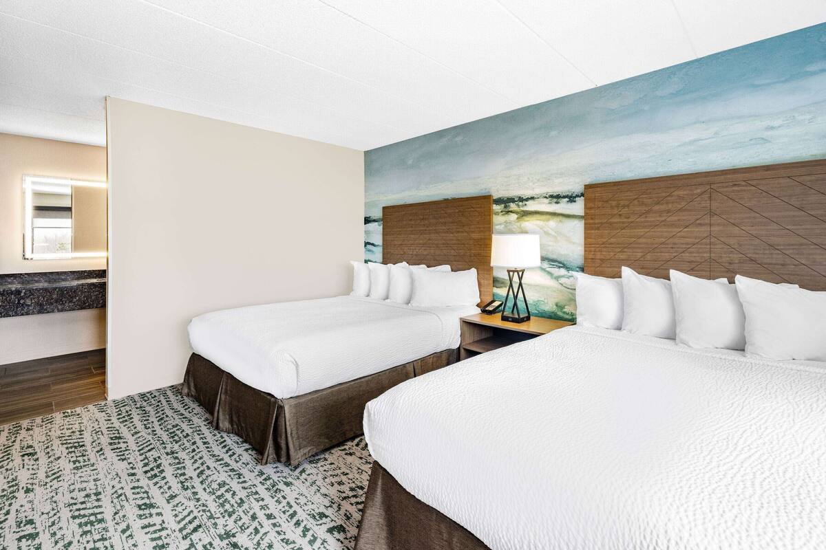 Hotelkamer met twee bedden, een nachtkastje met lamp, een schilderij aan de muur en een badkamer door een open deur.