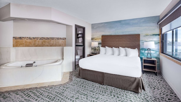 Une chambre d’hôtel moderne dotée d’un grand lit, d’une baignoire intégrée, d’une vue sur la ville et d’une fresque murale.