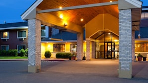 L’entrée d’un hôtel, avec un passage couvert, des piliers en briques et une porte en verre donnant sur l’intérieur.