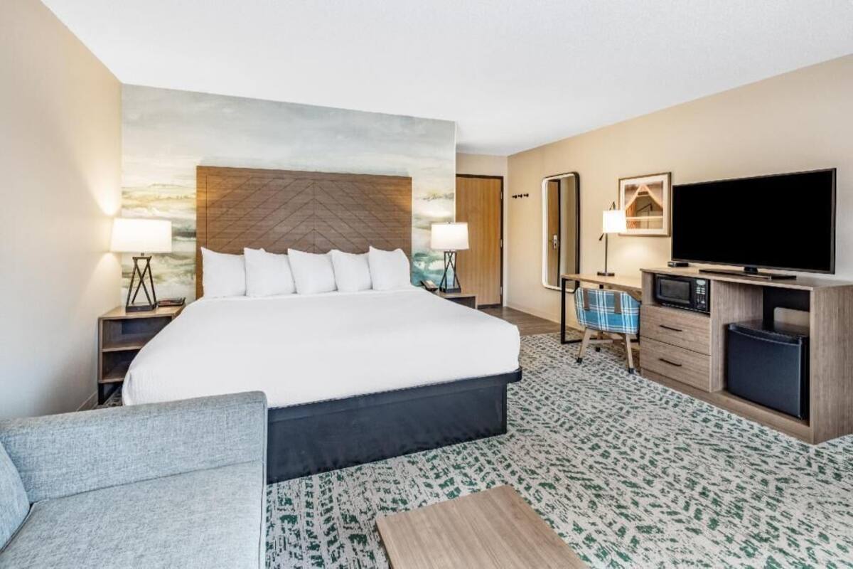 Een hotelkamer met een groot bed, een flatscreen televisie, een bureau met een computer, een stoel en een kleine tafel.