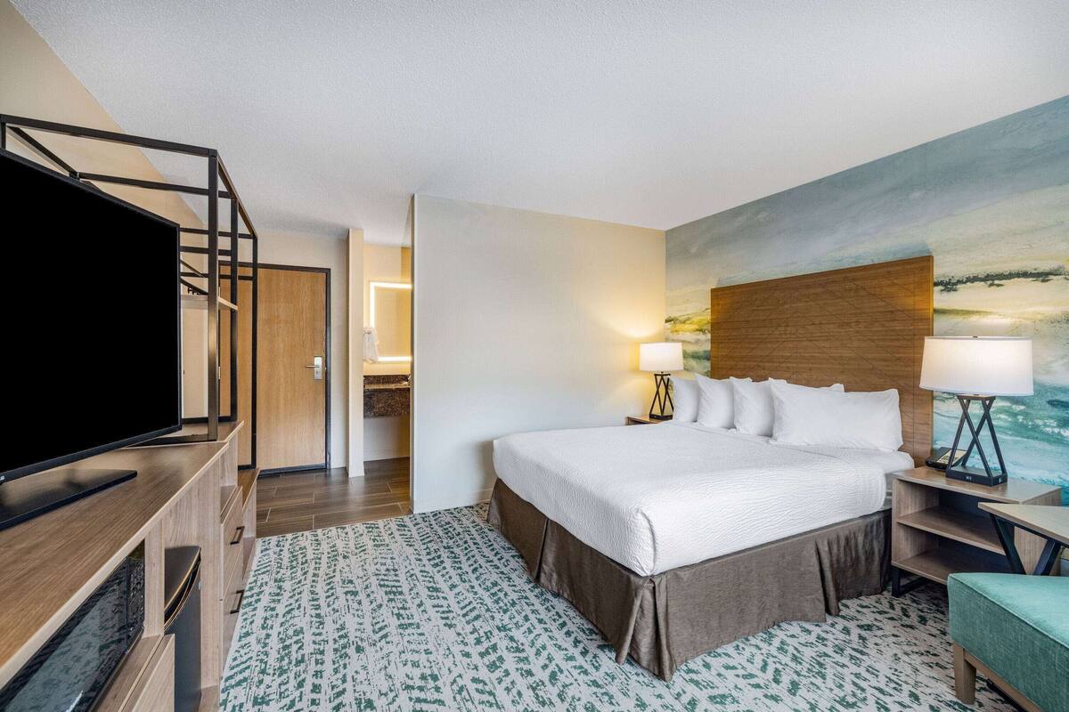 Een hotelkamer met een groot bed, een televisie, een schilderij aan de muur en een bureau met een lamp.
