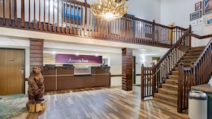 Un hall d’entrée avec un comptoir de réception portant l’inscription « American Inn », un escalier en bois et une sculpture d’ours décorative.