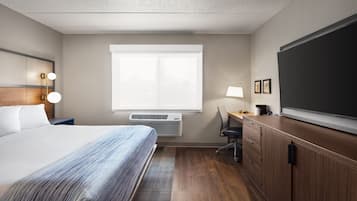 Une chambre d’hôtel équipée d’un lit, d’un bureau, d’une chaise, d’un grand téléviseur à écran plat et d’une fenêtre avec des stores.