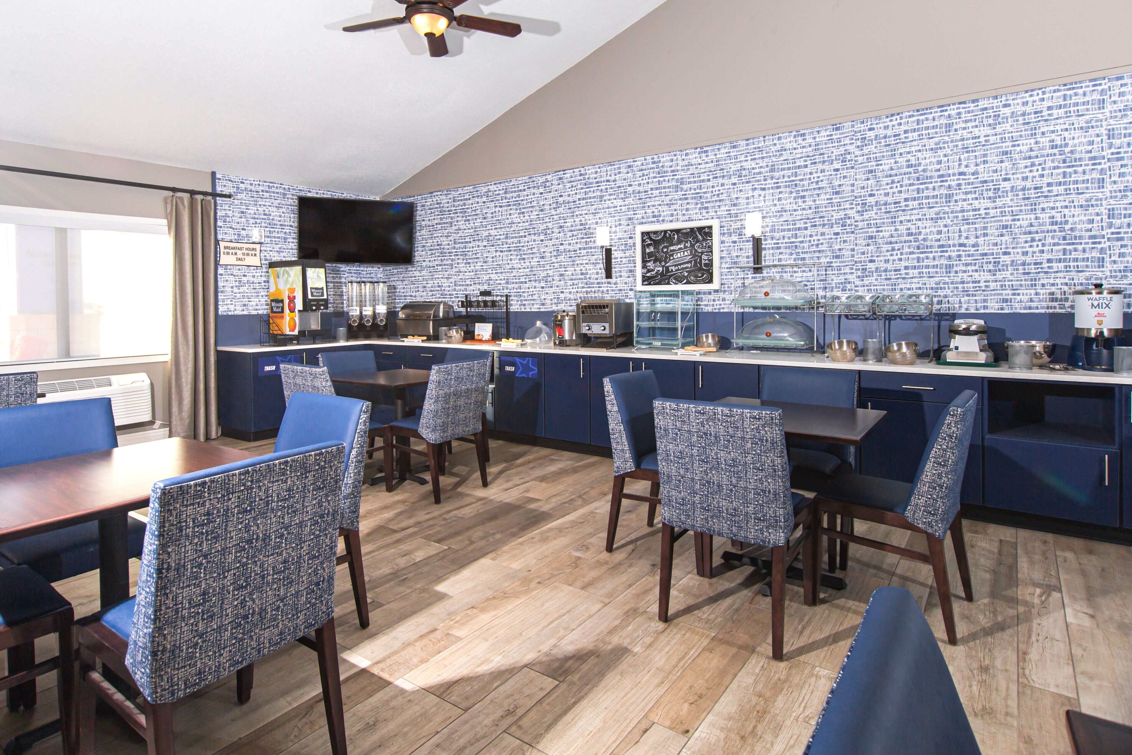 A restaurant with blue chairs, a counter with food items, and a television mounted on the wall.