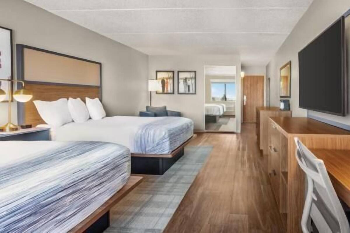A hotel room with two beds, a TV, a desk, and a view of the city.