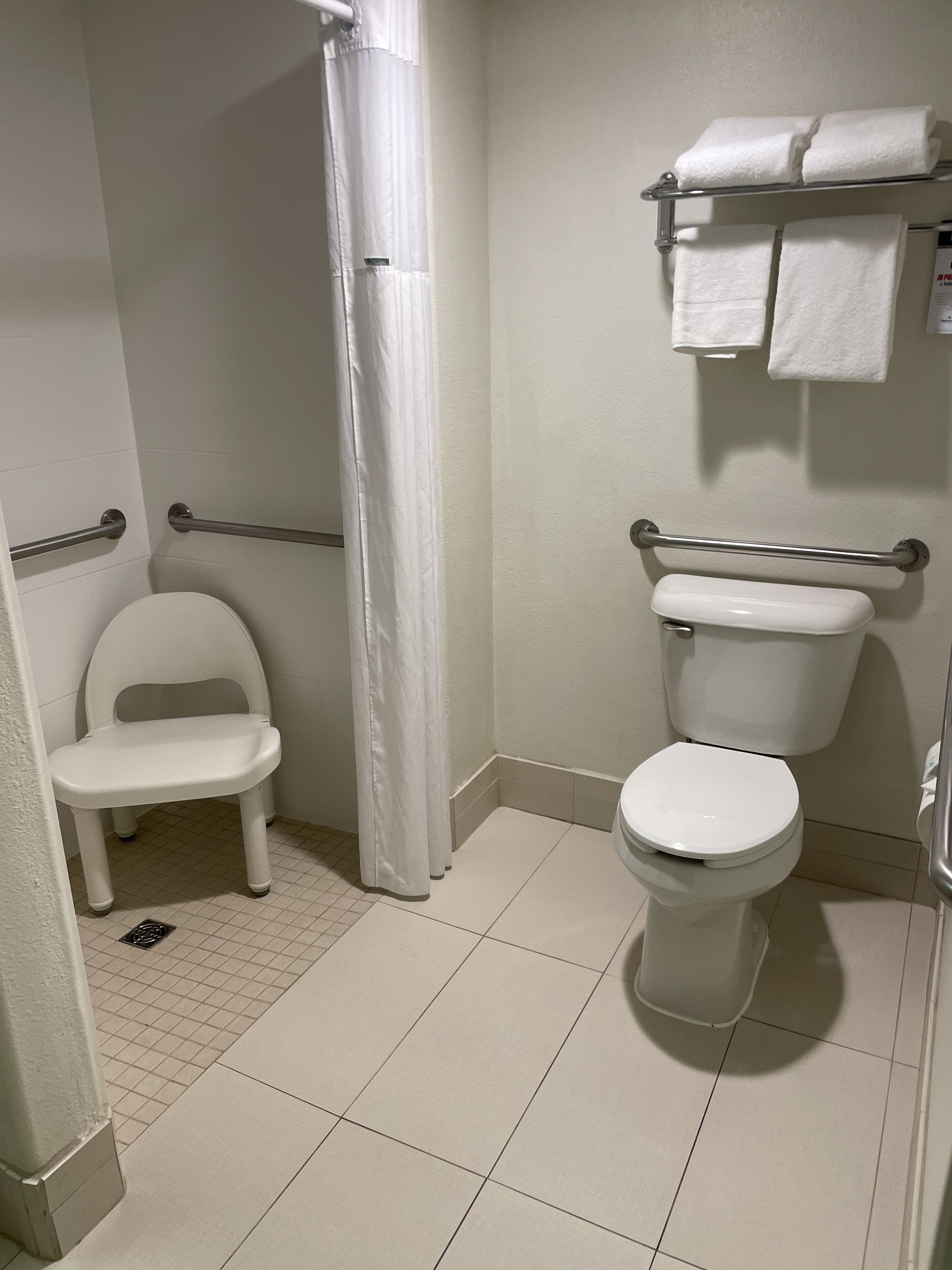 A small, clean bathroom with a toilet, a shower curtain, a grab bar, and a small stool.