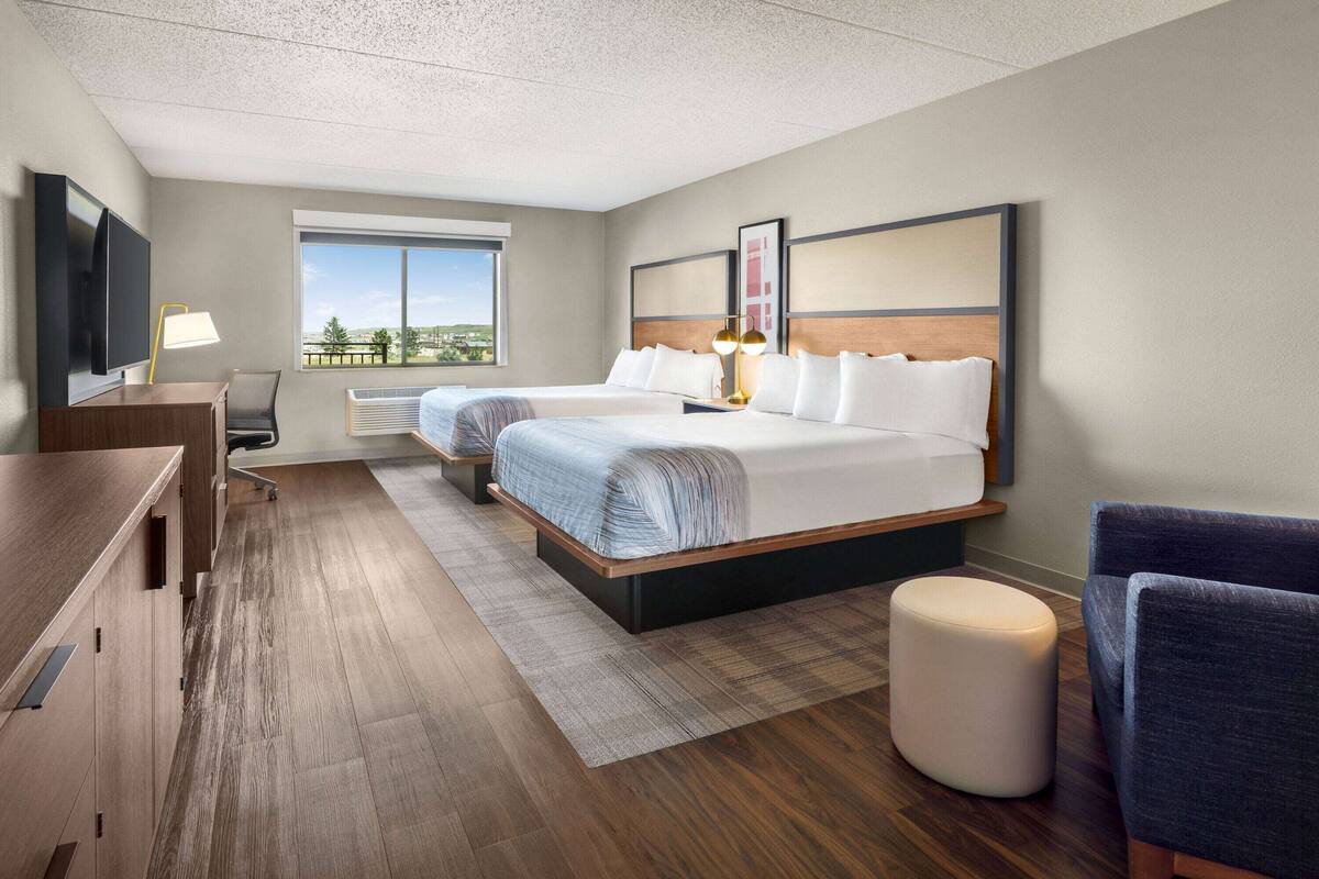 A hotel room with two beds, a desk, a chair, and a TV.