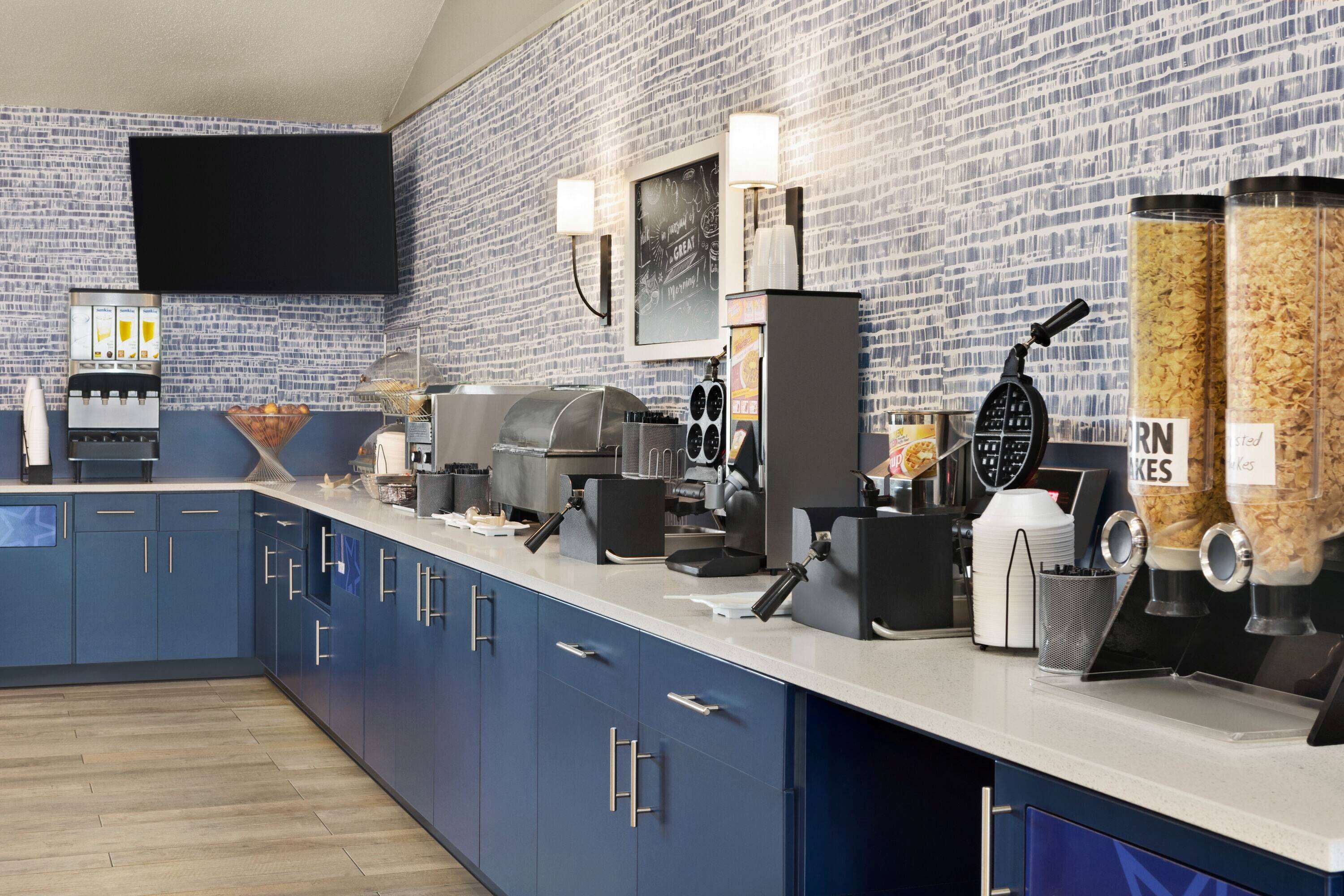 A modern kitchen with blue cabinets, a coffee machine, a waffle maker, and a chalkboard menu.