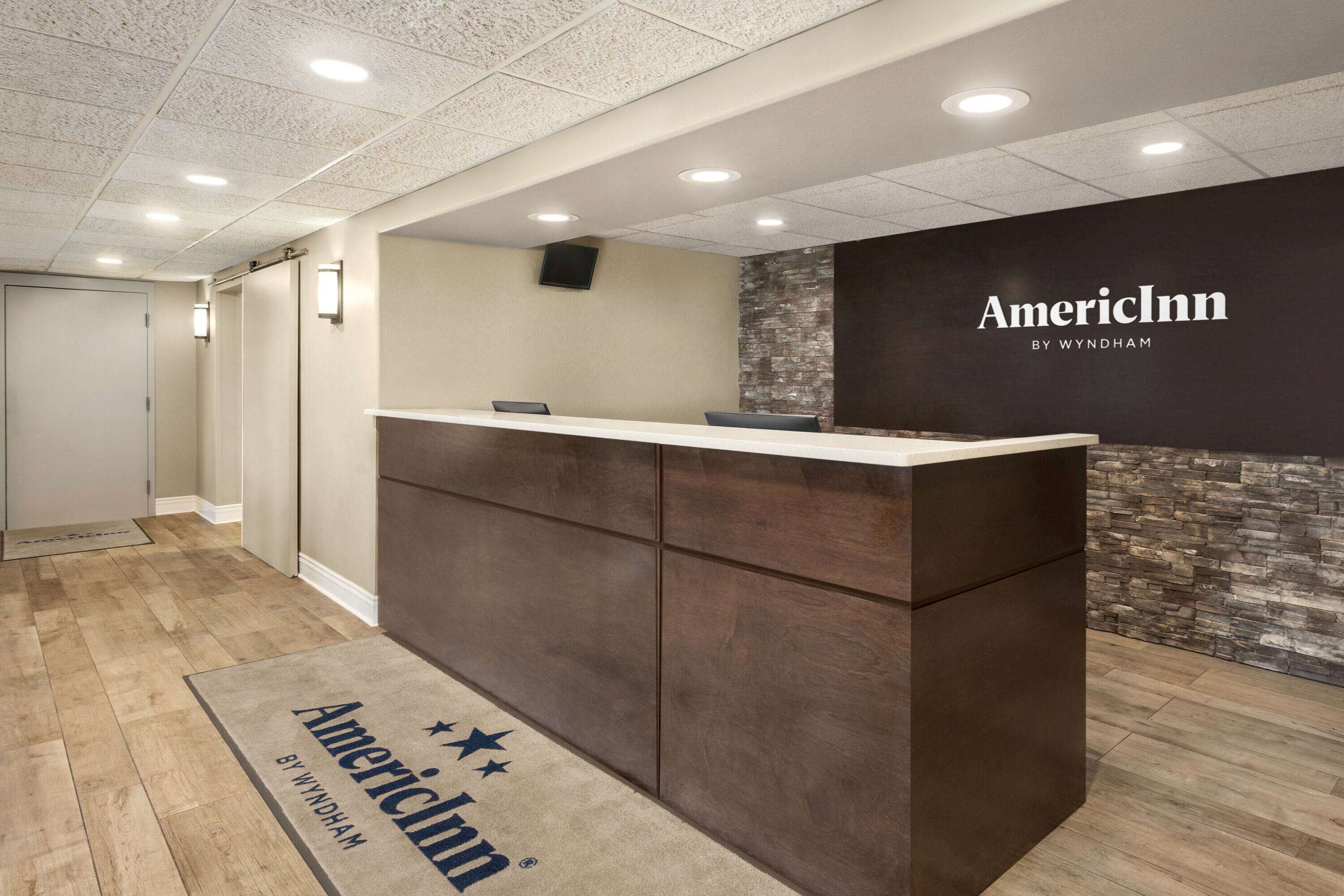 Een receptiezone met een houten vloer, een receptiebalie en een muur met het AmericInn logo.