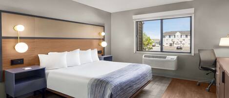 Ett modernt hotellrum med en stor säng, sängbord med lampor, utsikt över omgivningarna genom ett fönster och ett skrivbord med en stol.