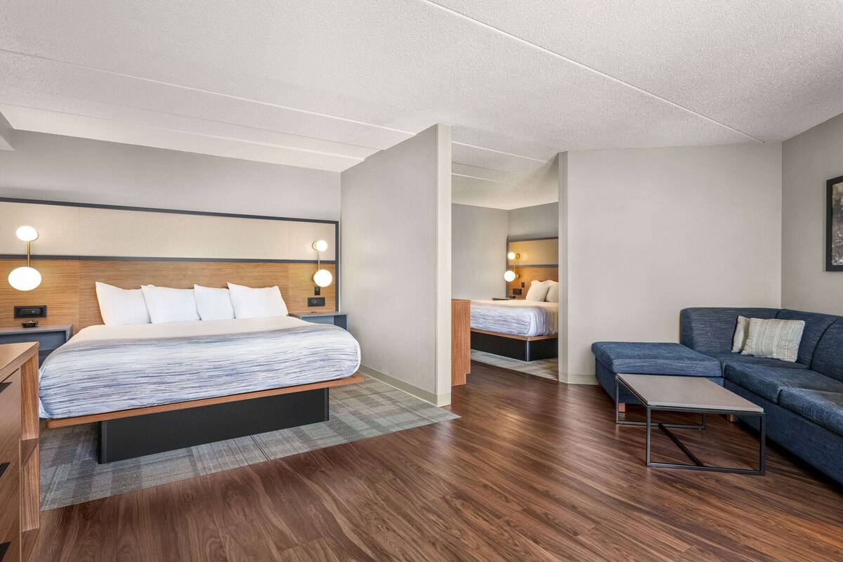A modern hotel room with a large bed, a sofa, a small table, and a nightstand.