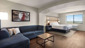 A modern hotel room with a sofa, a bed, a bedside table, a lamp, and a large window offering a view.