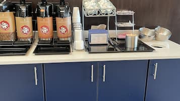 Un espace dédié au café, équipé de distributeurs à l’effigie de la marque, d’une machine à café et d’un présentoir rempli de gobelets jetables.