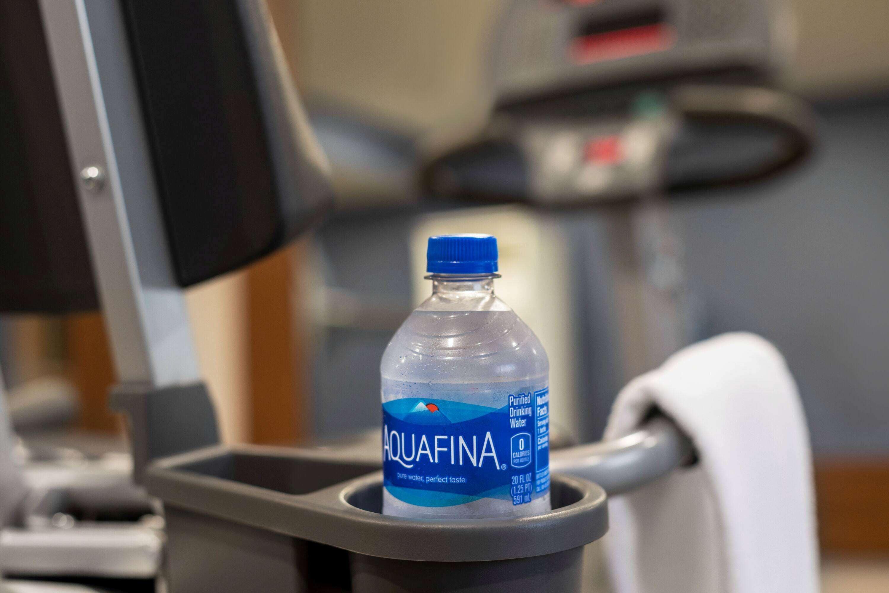 A bottle of Aquafina water in a gray dispenser on a gym equipment.