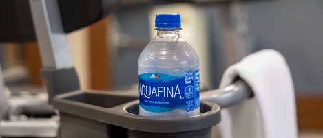 Una botella de agua Aquafina en un dispensador gris sobre equipo de gimnasio.