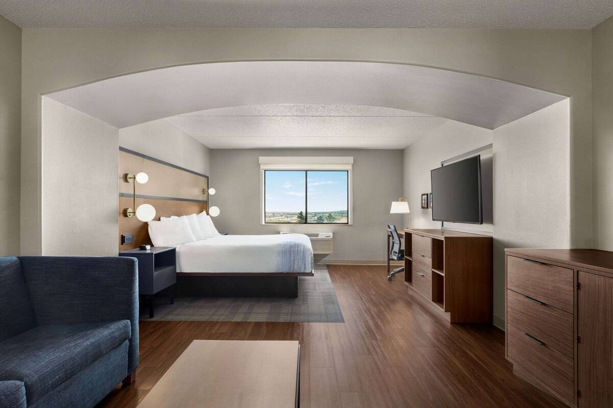 A hotel room with a large bed, a TV, a desk, and a view of the outdoors.