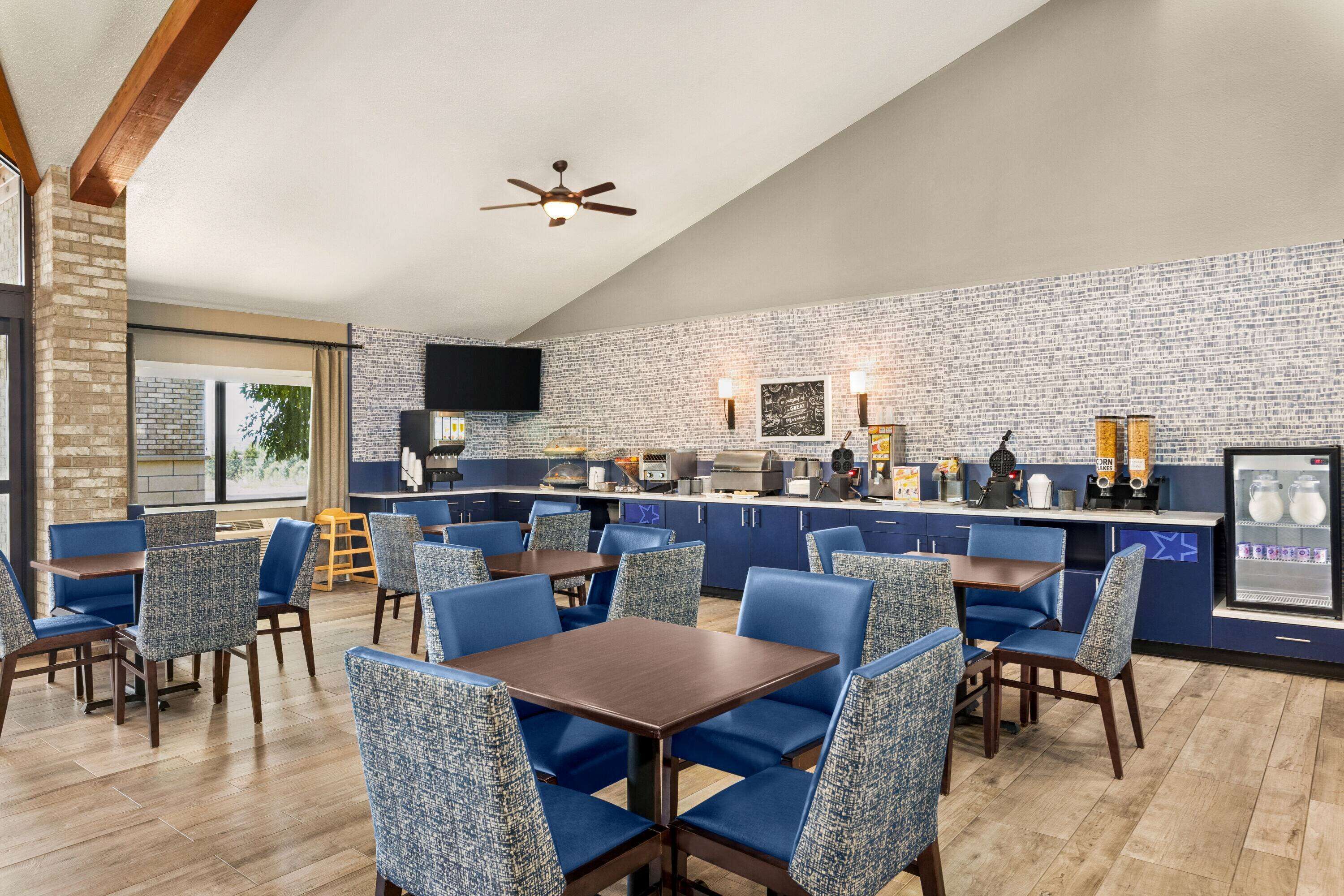 A restaurant with blue upholstered chairs, a wooden table, a brick wall, and a ceiling fan.