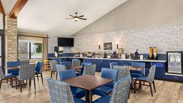 A restaurant with blue upholstered chairs, a wooden table, a brick wall, and a ceiling fan.