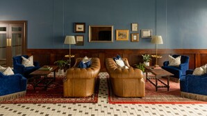 A room with two leather armchairs, a wooden coffee table, and a patterned rug. There are framed pictures on the wall and two lamps.