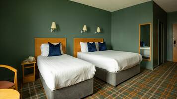 A hotel room with two beds, a small table, a chair, and a mirror.
