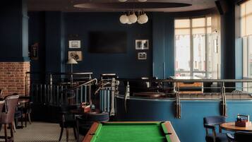 A billiards room with a pool table, chairs, and a brick wall.