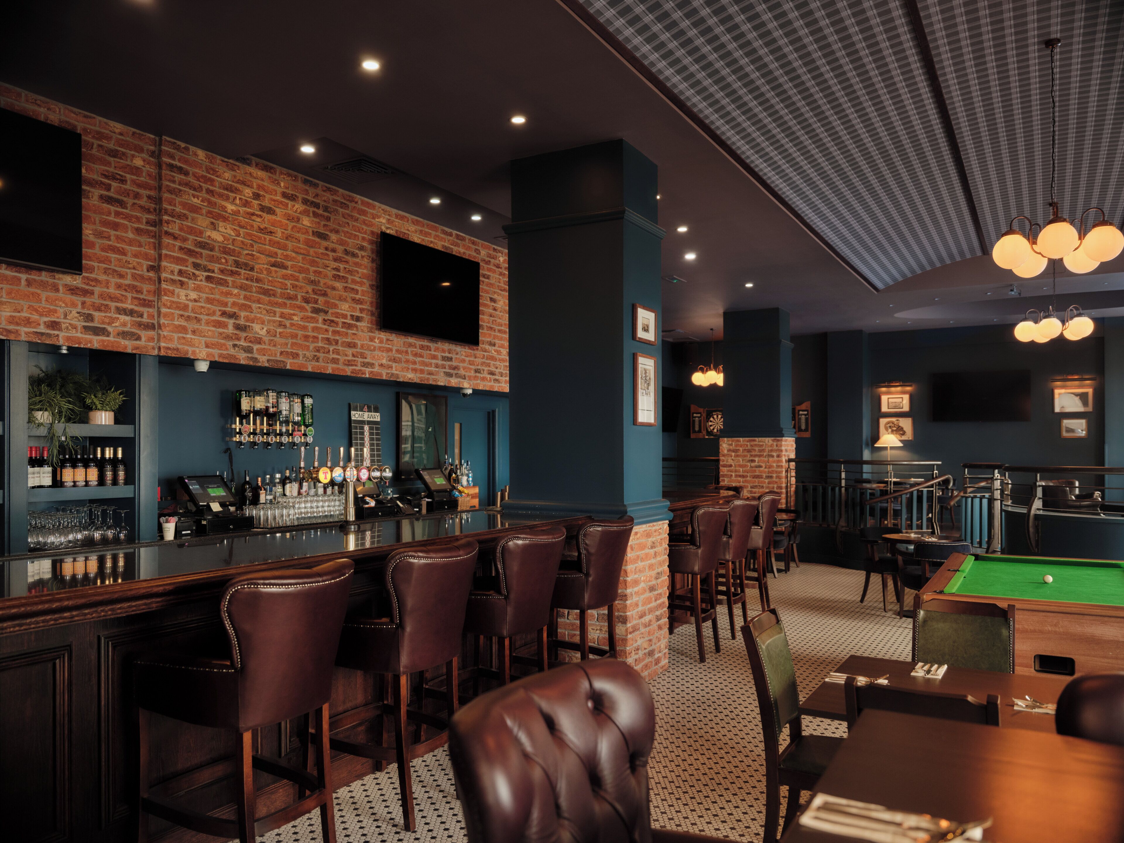 A bar area with a brick wall, bar stools, a pool table, and a billiards table.