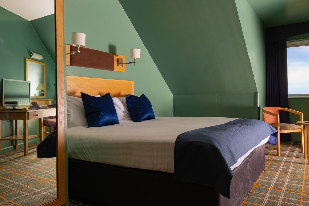 Una habitación de hotel con cama, escritorio, silla y ventana.