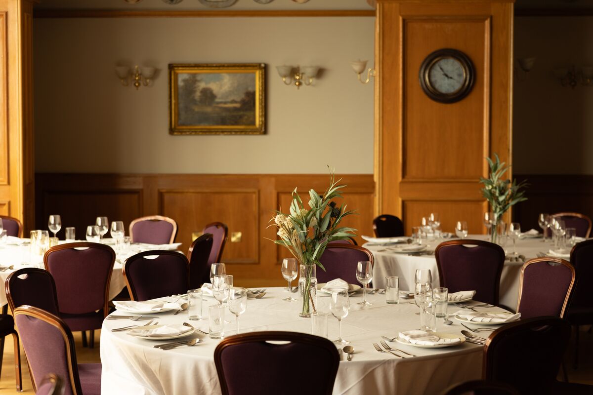 A dining room with round tables set for a meal, chairs, and a clock on the wall.