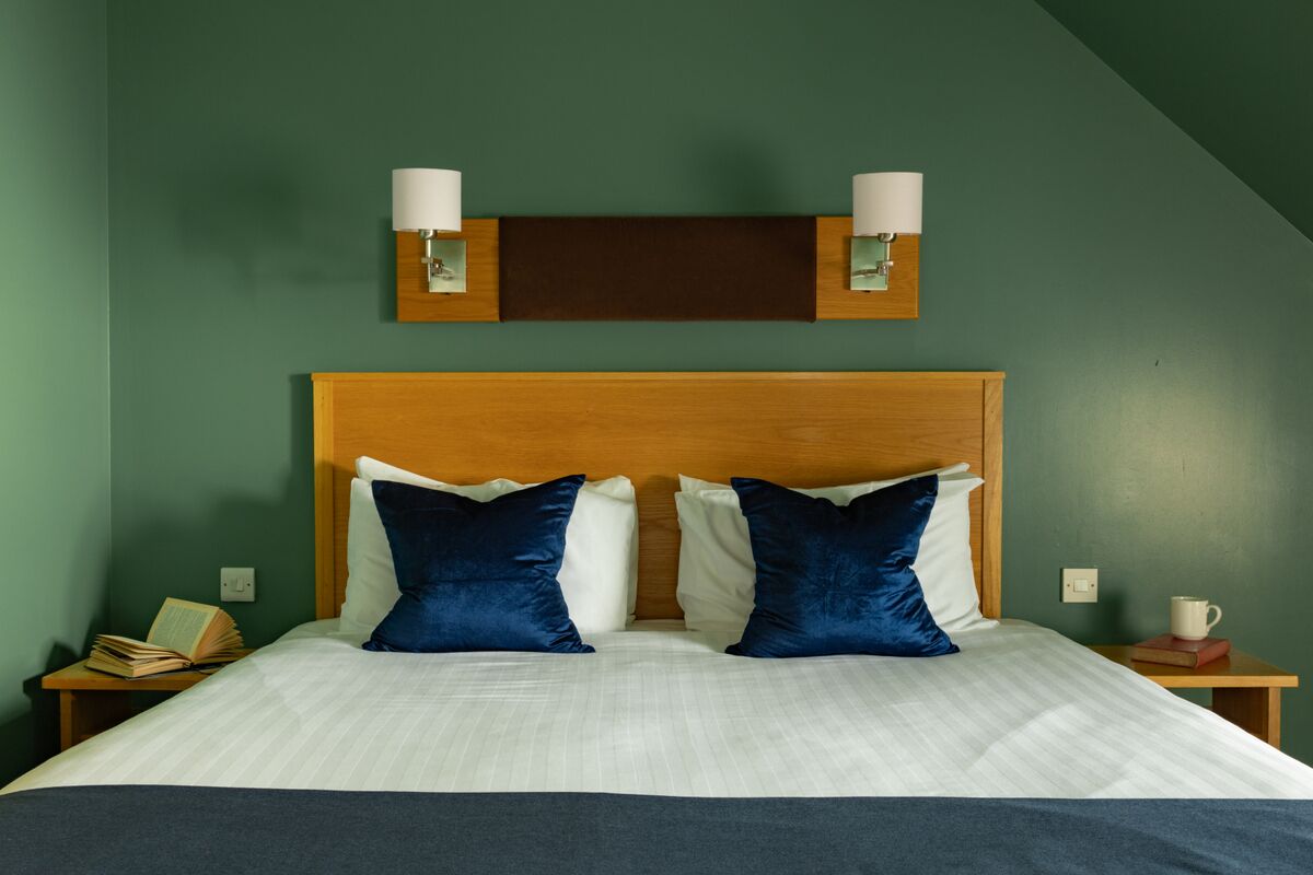 Una cama bien hecha con dos almohadas, un cabecero de madera y dos lámparas fijadas a la pared.