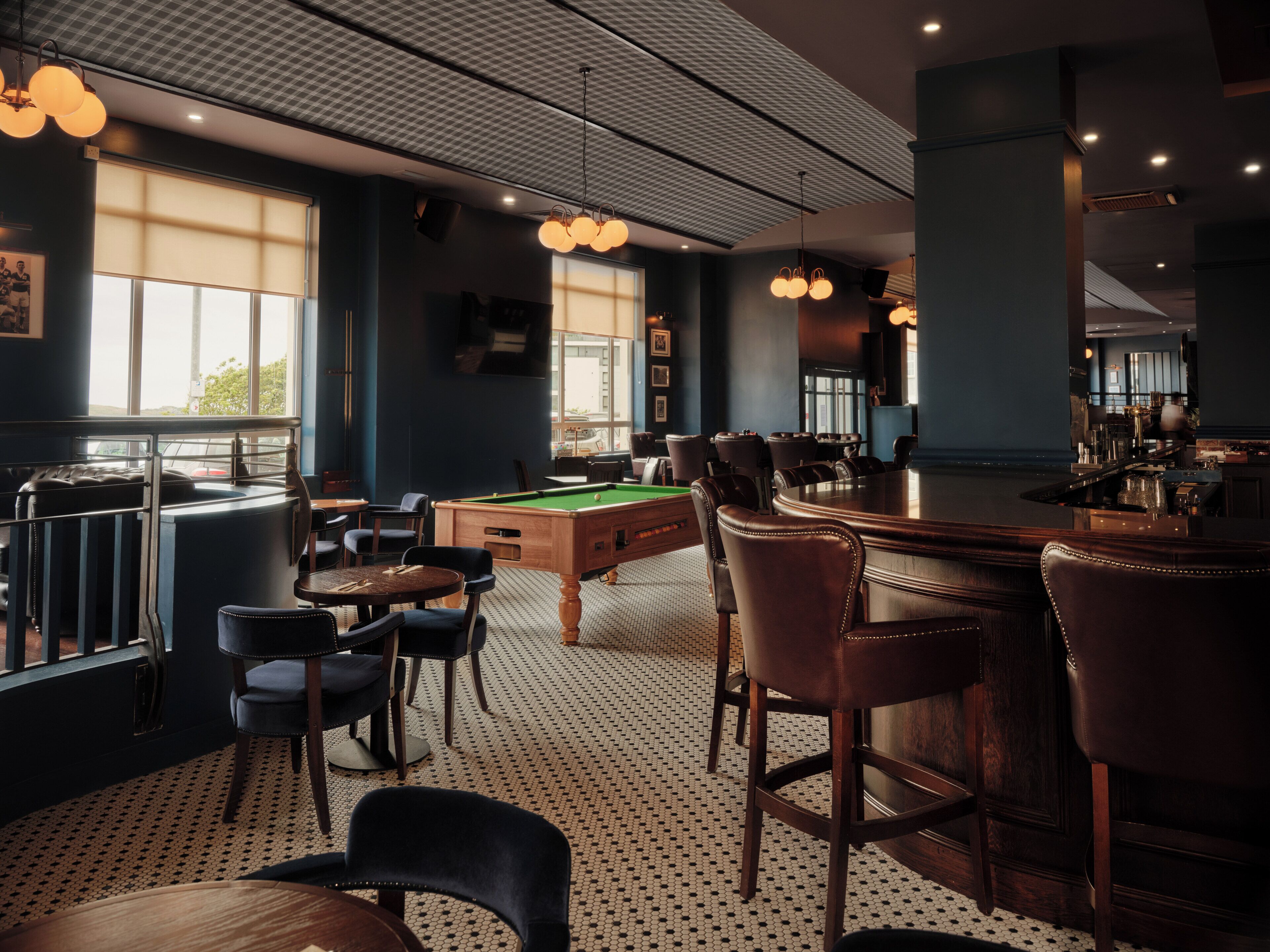 A billiards room with a pool table, bar area, and seating.