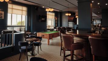 A billiards room with a pool table, bar area, and seating.