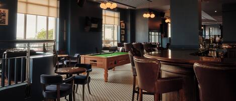 A billiards room with a pool table, bar area, and seating.