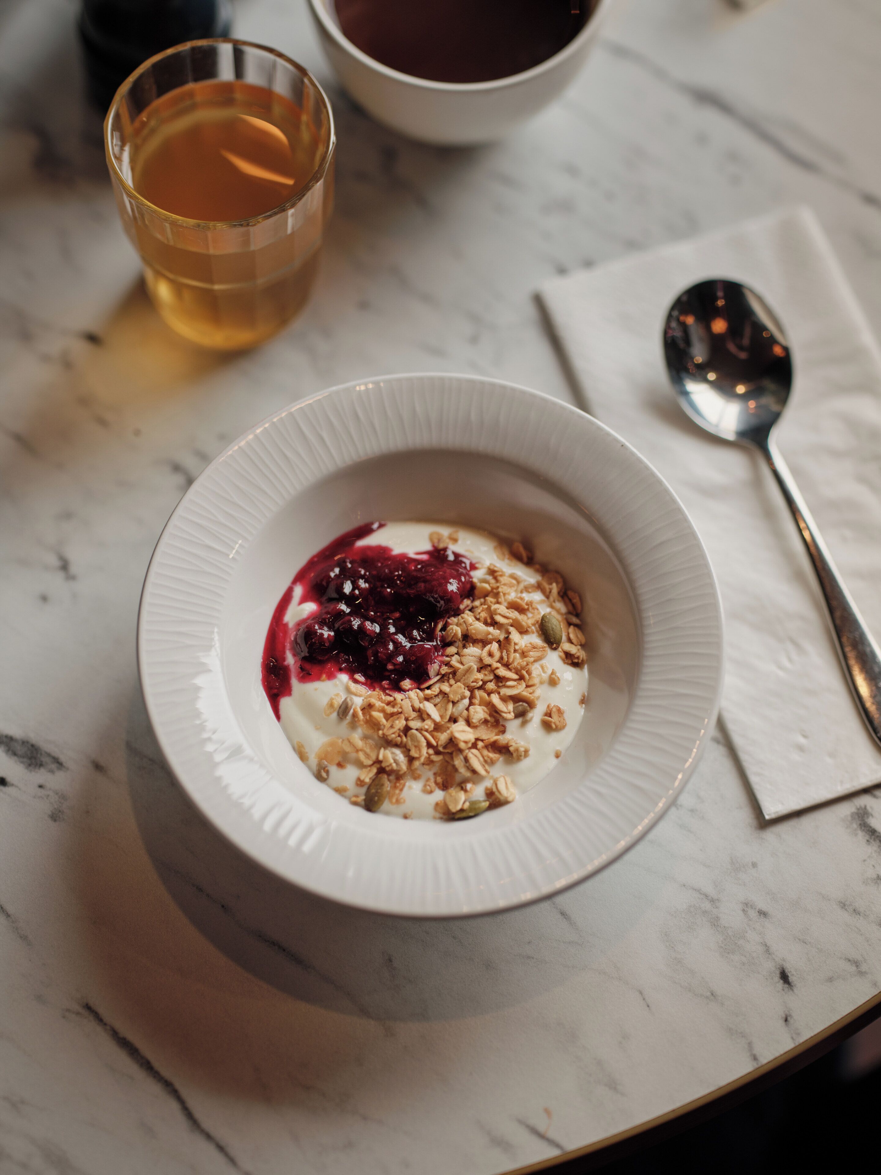 Kulho jogurttia, johon on lisätty mysliä ja marjakompottia, on asetettu marmoripöydälle.