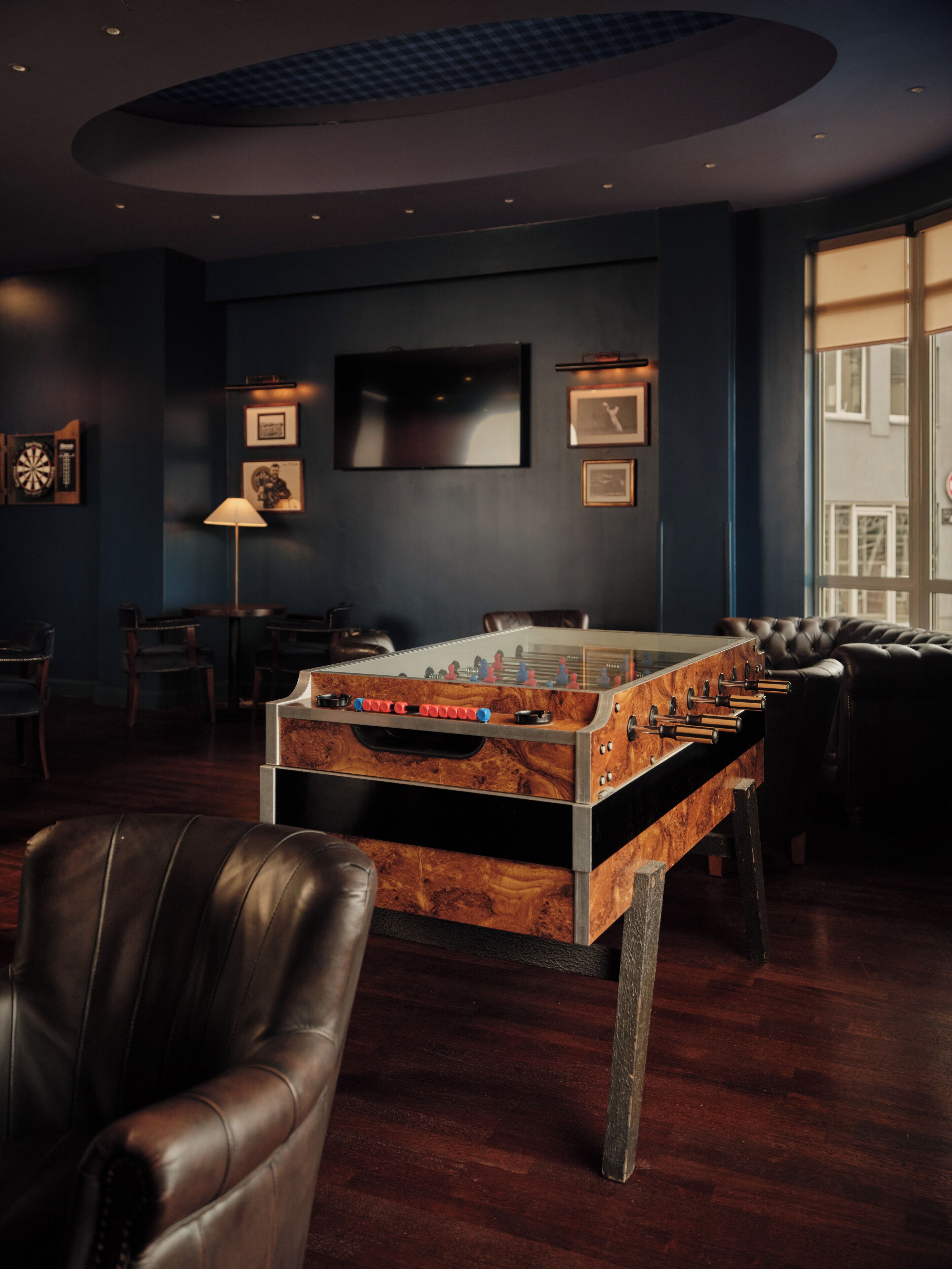 Une pièce avec un baby-foot, des fauteuils en cuir, un téléviseur à écran plat et des tableaux encadrés accrochés au mur.