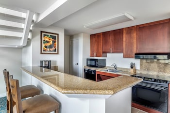 A modern living room with a sofa, armchair, and coffee table. A kitchen area with a dining table and chairs is visible in the background. at Hilton Grand Vacations Club at Hilton Hawaiian Village