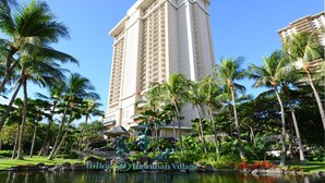 A tall hotel with a pool surrounded by palm trees and a statue.