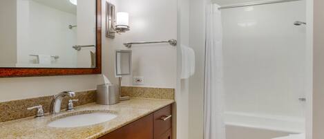 A bathroom with a sink, mirror, towel rack, and a shower area.