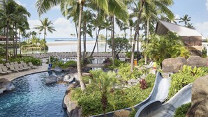 A resort pool area with a water slide, lounge chairs, and palm trees. - Hilton Grand Vacations Club at Hilton Hawaiian Village (Honolulu)