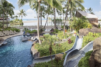 A beachfront hotel with multiple high-rise buildings, palm trees, and a sandy beach. at Hilton Grand Vacations Club at Hilton Hawaiian Village