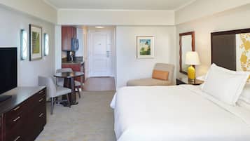 A hotel room with a bed, a desk, a chair, a TV, a lamp, and a painting on the wall.