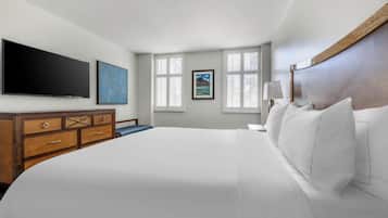 Habitación de hotel con una cama grande, un televisor de pantalla plana, un aparador de madera y dos ventanas con persianas.