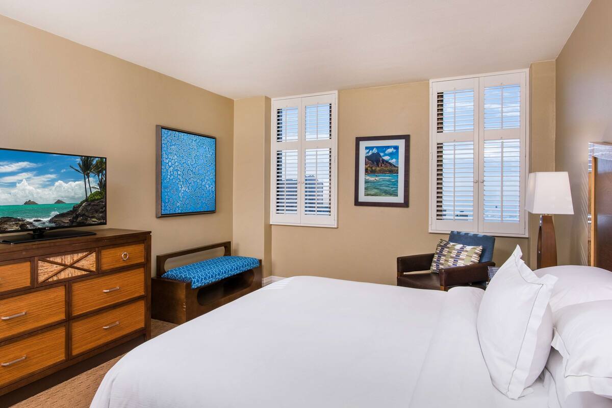 Ein Hotelzimmer mit einem großen Bett, einem hölzernen Schminktisch, einer Bank und einem Fernseher auf dem Schminktisch.