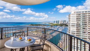 A balcony with a table and chairs, overlooking a marina with boats and a beach. - Hilton Grand Vacations Club at Hilton Hawaiian Village (Honolulu)