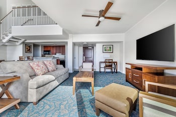 A hotel room with a large bed, a dresser, a desk, a chair, and a view of the city through a large window. at Hilton Grand Vacations Club at Hilton Hawaiian Village