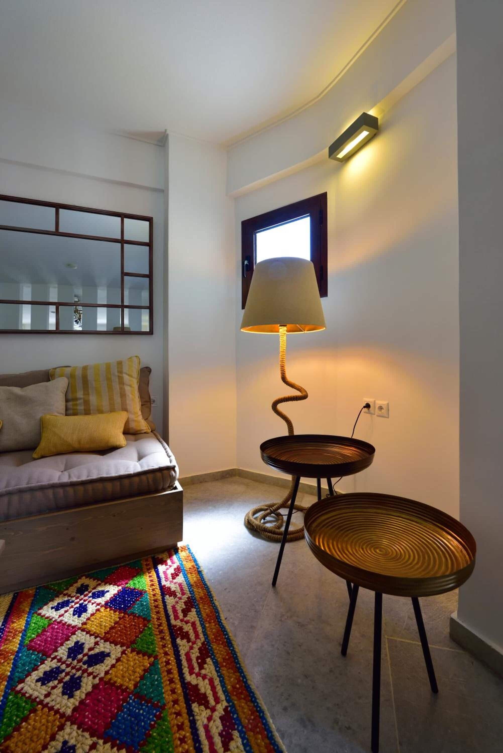 Un dormitorio con una cama, un tapete colorido, una lámpara y una mesita.